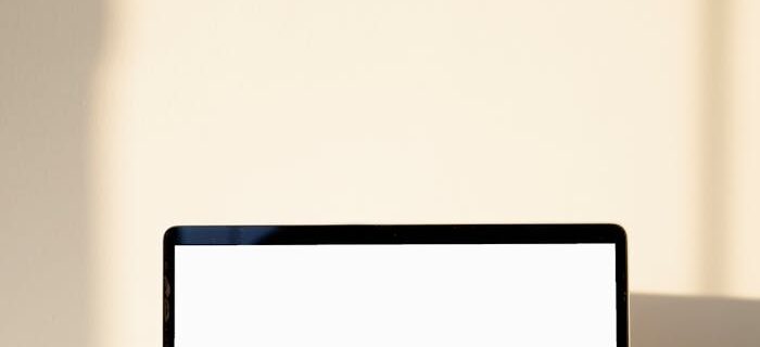 A sleek laptop with a blank screen, perfect for mockups, set against a sunlit wall for a minimalist aesthetic.